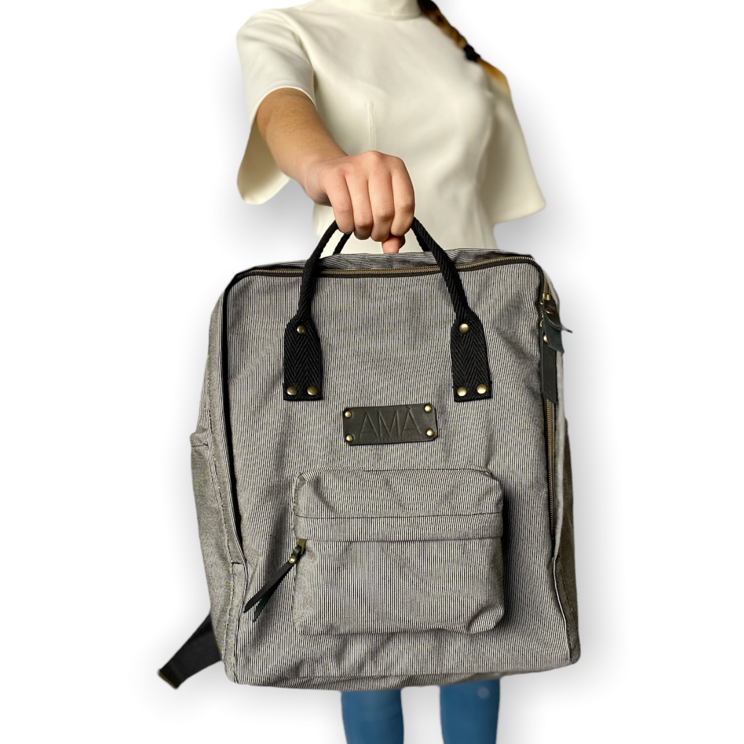 La mochila Alexa está hecha con tejido impermeable de rayas muy finas negras y blancas y con dos cintas negras en cinta de algodón regulables. En la parte superior tiene dos asas con un botón para proteger mejor su contenido. También tiene un bolsillo delantero donde podrás guardar las cosas para tenerlas más a mano y un bolsillo a cada lado para que puedas guardar el paraguas, la botella de agua…