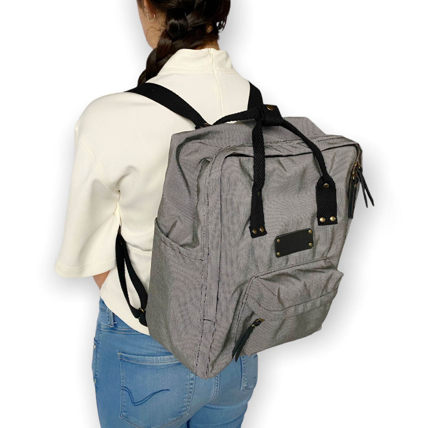 La mochila Alexa está hecha con tejido impermeable de rayas muy finas negras y blancas y con dos cintas negras en cinta de algodón regulables. En la parte superior tiene dos asas con un botón para proteger mejor su contenido. También tiene un bolsillo delantero donde podrás guardar las cosas para tenerlas más a mano y un bolsillo a cada lado para que puedas guardar el paraguas, la botella de agua…