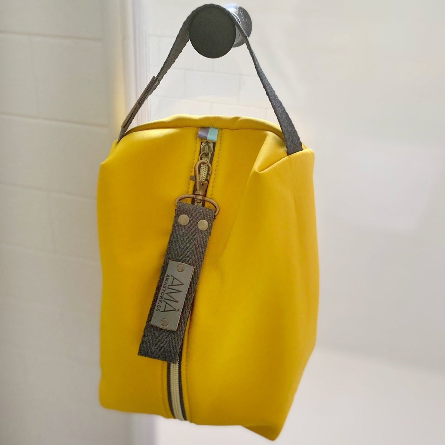 Neceser de tejido de neopreno color Amarillo con una práctica asa de algodón color natural que te permitirá colgar el neceser del pomo de la puerta o cualquier colgador. Están realizados mano en Barcelona y disponen de forro repelente al agua y bolsillo interior. El tirador de la cremallera se convierte en un llavero extraible. Además puedes escoger personalizar tu neceser con 2 iniciales.