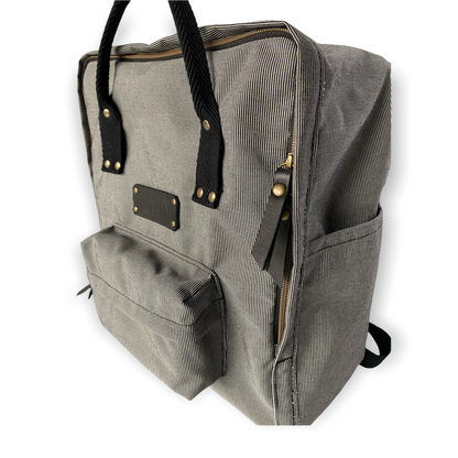 La mochila Alexa está hecha con tejido impermeable de rayas muy finas negras y blancas y con dos cintas negras en cinta de algodón regulables. En la parte superior tiene dos asas con un botón para proteger mejor su contenido. También tiene un bolsillo delantero donde podrás guardar las cosas para tenerlas más a mano y un bolsillo a cada lado para que puedas guardar el paraguas, la botella de agua…