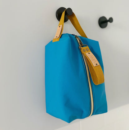 Neceser de tejido de neopreno color Azul con una práctica asa de algodón color natural que te permitirá colgar el neceser del pomo de la puerta o cualquier colgador. Están realizados mano en Barcelona y disponen de forro repelente al agua y bolsillo interior. El tirador de la cremallera se convierte en un llavero extraible.  Además puedes escoger personalizar tu neceser con 2 iniciales.