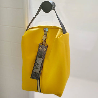 Neceser de tejido de neopreno color Amarillo con una práctica asa de algodón color natural que te permitirá colgar el neceser del pomo de la puerta o cualquier colgador. Están realizados mano en Barcelona y disponen de forro repelente al agua y bolsillo interior. El tirador de la cremallera se convierte en un llavero extraible.  Además puedes escoger personalizar tu neceser con 2 iniciales.